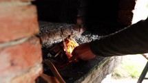 Person's hand lighting a matchstick in an outdoor brick fireplace.