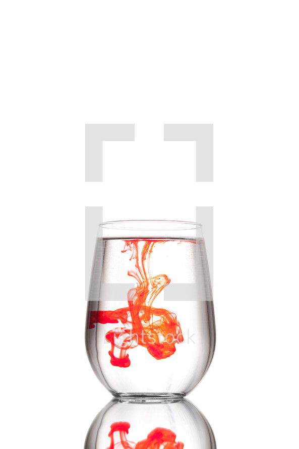 A single red drop in a clear glass of water against a white background.