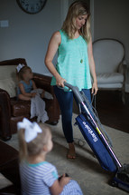 a mother vacuuming while daughters watch tv 
