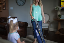 a mother vacuuming while daughter watches tv 