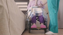Young nurse caring of elder disabled woman in wheelchair and going for a walk. Home or hospice nursing and assistance concept.