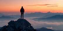 Silhouette of a man standing on top of a mountain and looking at the sunrise