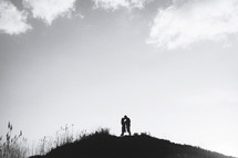 a couple kissing at the top of a hill 