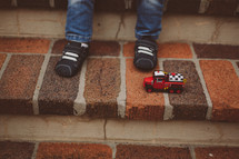 toddlers feet and a toy firetruck on steps