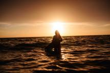 silhouette of a female surfer in the ocean at sunset 