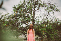 a woman standing outdoors near an orange tree 
