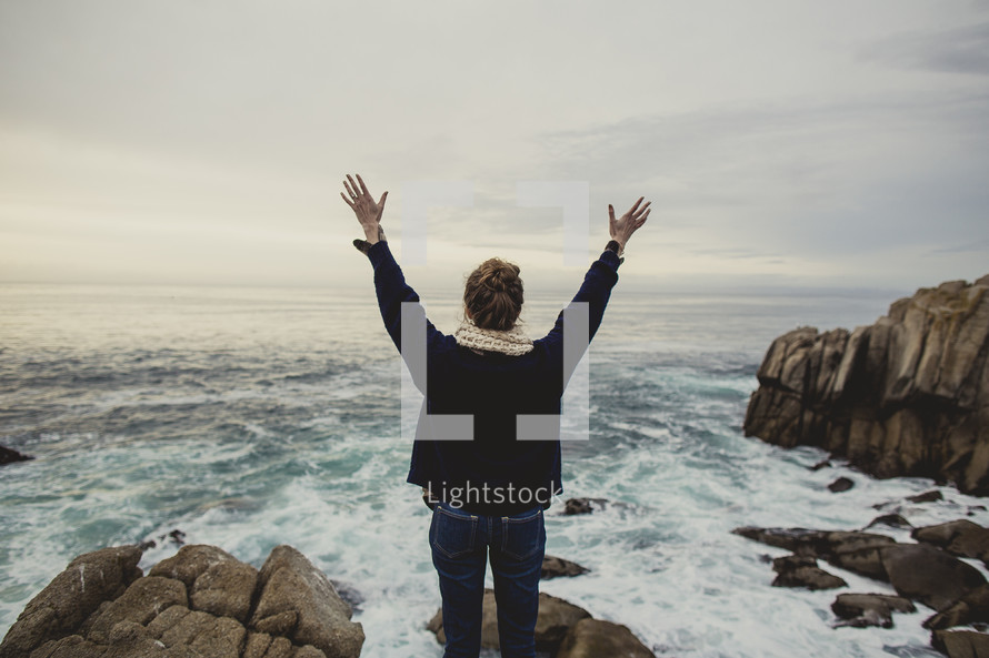 woman standing at the edge of the ocean with her arms raised