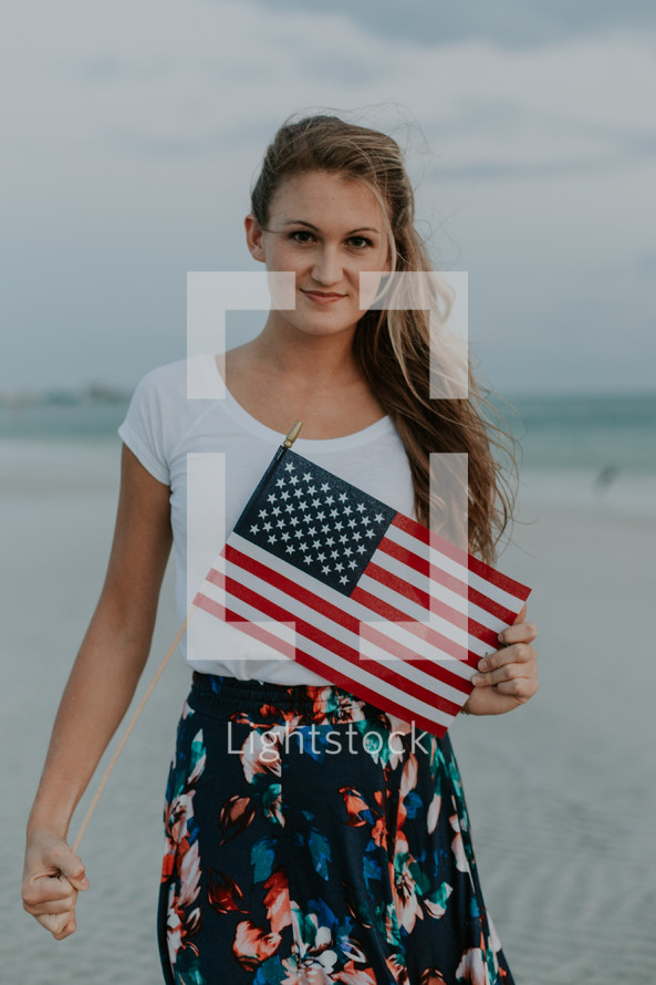 a young woman walking on a beach carrying an American flag 