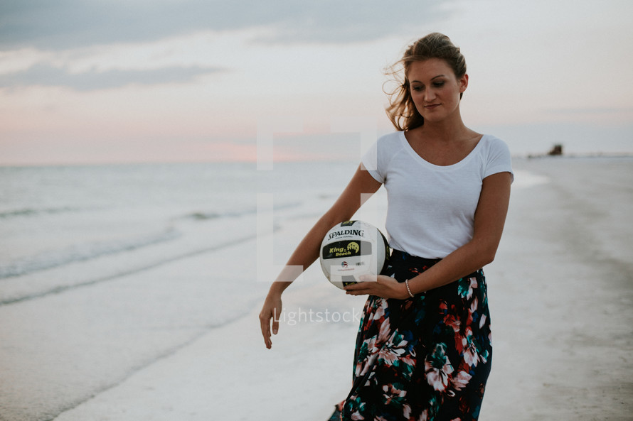 a young woman walking on a beach carrying a volleyball 