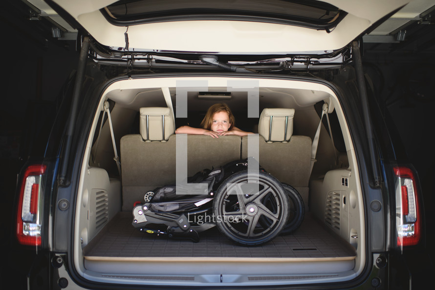 a child looking over the backseat and a stroller in the trunk of an SUV 