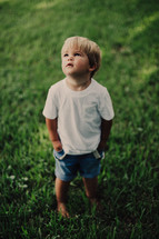 a toddler boy standing in the grass 