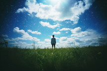 Back view of a man standing in the middle of the field and looking at the sky