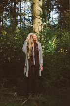 a woman standing alone in a forest touching her blonde hair 