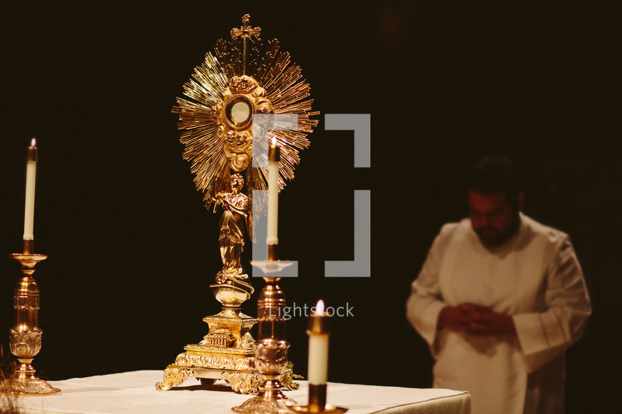 Priest bowing before the Monstrance at Eucharist adoration in a Catholic church .