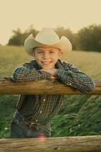A smiling boy leaning on a fence.