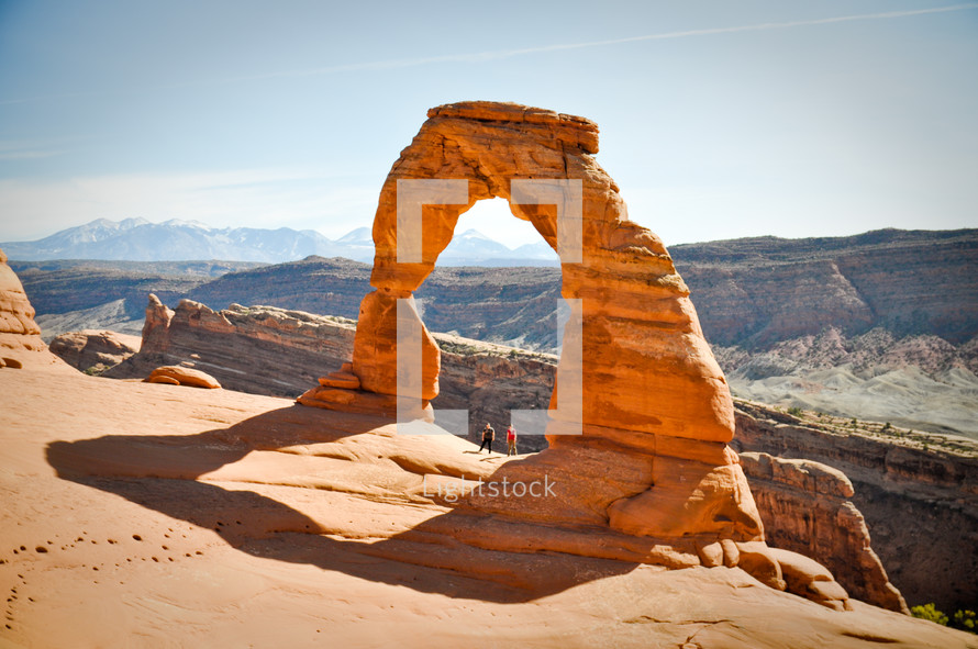 Two hikers stand under the Delicate Arch in Moab, Utah.