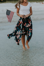 a young woman walking on a beach carrying an American flag 