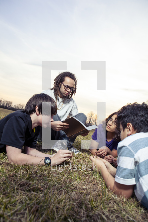 A young man reading a Bible to a group of children 