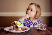 a child decorating and tasting a gingerbread house 