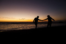 silhouette of a couple walking holding hands on a beach at sunset relationship engagement marriage love man woman