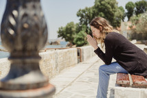 woman saying a prayer sitting on a bench in Greece 