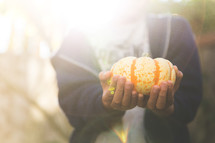 person holding a striped pumpkin in bright sunlight 