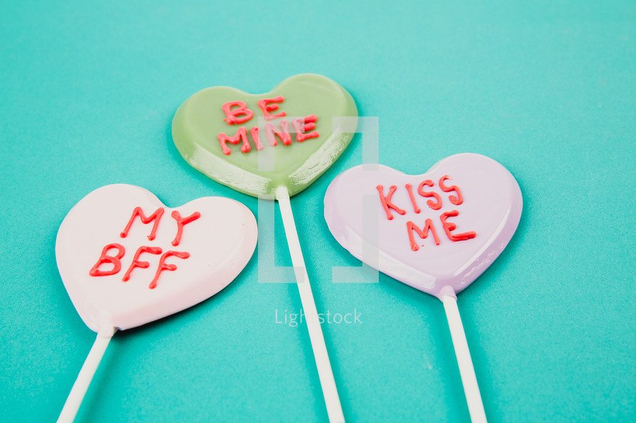 Candy hearts on a stick with Valentine messages on an aqua background.