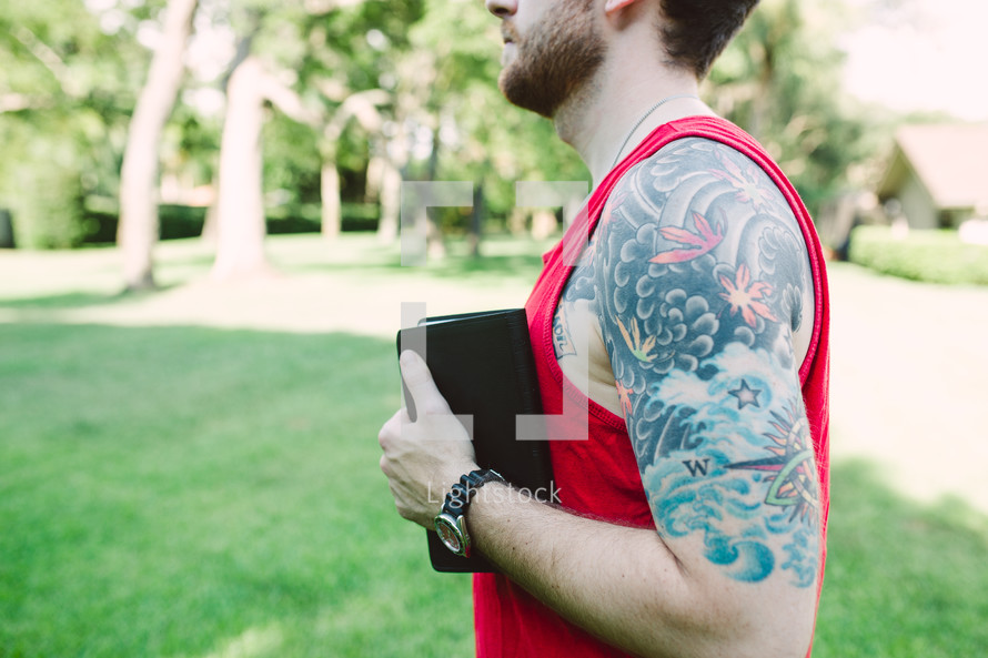 man with tattoos holding a Bible 