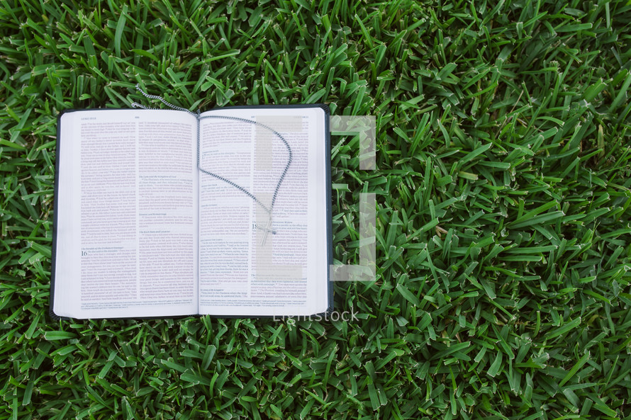 open Bible with a cross necklace in the grass 