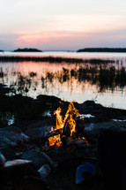 sitting by a campfire by a lake at dusk 