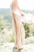A woman in a gauzy dress standing on the edge of a cliff.