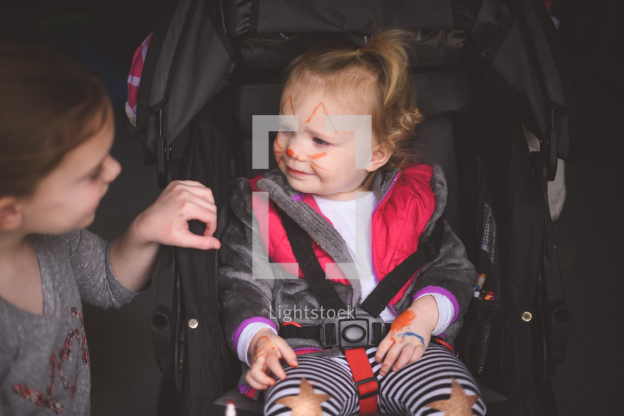 toddler with face paint in a stroller 