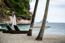 A hammock between palm trees on a beach by the sea.