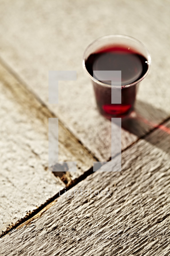 A communion cup filled with wine sits on a wooden table