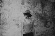 a woman in a hat and tank top standing in front of a grungy wall 