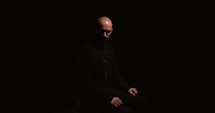 Push in on bald man in black with dark background