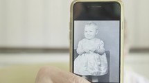 Senior caucasian woman holding a smartphone to the camera with an image of her self as a child then lowering the phone to reveal herself behind themes of technology memories childhood nostalgia