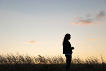 a teen girl praying outdoors in a field at sunset 