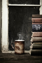 Steaming hot cup of coffee sitting on wood table next to a stack of books