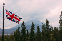 British flag on a flagpole in front of a forest 