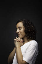 a side profile of a praying teen girl against a black background 