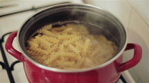 Red pot with pasta on gas stove.