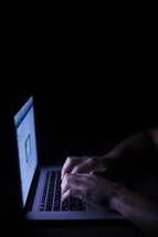 a man typing and looking at a computer screen at night 