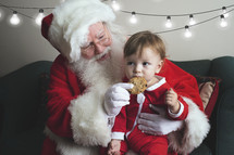 a toddler eating cookies on Santa's lap 