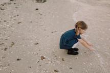 a toddler girl in a dress on a beach reaching for the ocean 