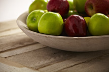 A bowl of green and red apples rest on a wooden table.