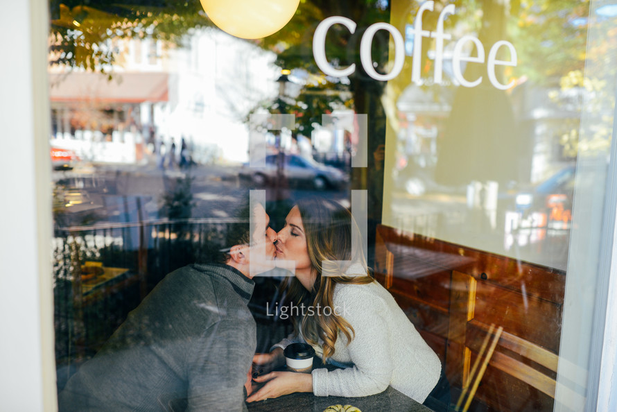 A couple kiss in the window of a coffee shop.