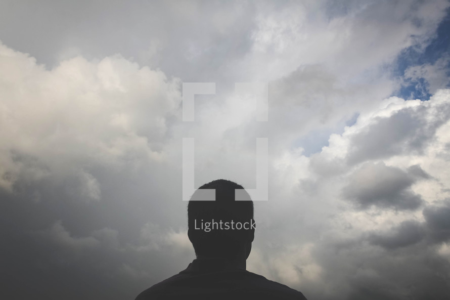 silhouette of a man looking up at clouds 