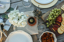 Place settings with fruits, nuts and flowers on a picnic table outside.