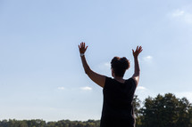 an African American woman with raised hands standing outdoors 